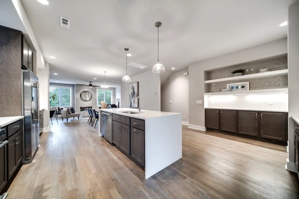 This image features a welcoming kitchen and living area, with a kitchen island illuminated by stylish pendant lights and a window view that hints at the world beyond. The space is open, filled with natural light, and designed for both socializing and unwinding.