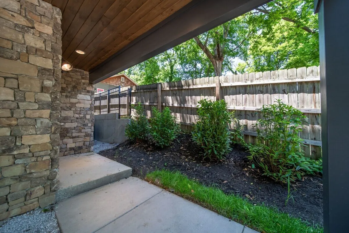 The image presents a tranquil exterior setting with a stone wall, paved walkway, and lush greenery. The space is ideal for relaxing mornings, casual gatherings, or simply soaking in the peaceful surroundings after a day exploring Nashville.