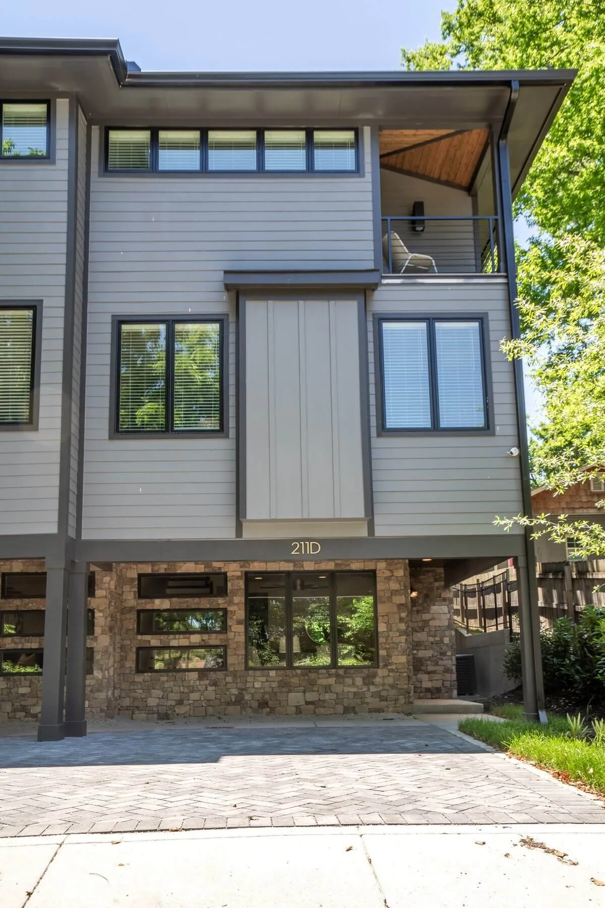 A distinctly modern exterior shot showcasing sleek architectural design, a stone base, generous windows, and a spacious balcony—ideal for social gatherings or relaxing outdoors. The setting evokes the blend of city living and personal comfort.