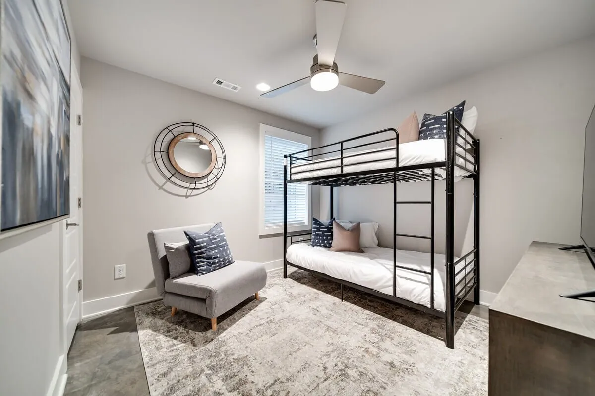 A cozy children's room with a bunk bed, plush armchair, mirrored wall, and a soft textured rug. The playful yet restful atmosphere is perfect for young travelers to unwind after a busy day.