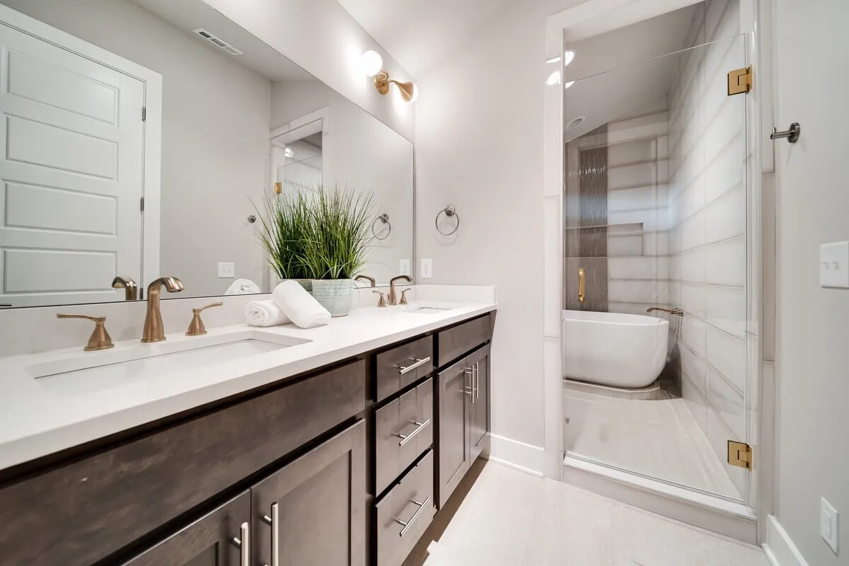 A modern, spa-inspired bathroom with a double vanity and stylish faucets, a freestanding bathtub, a large walk-in shower, and a decorative plant adding a touch of nature. The space is bright and airy, with a sense of luxury and calm.