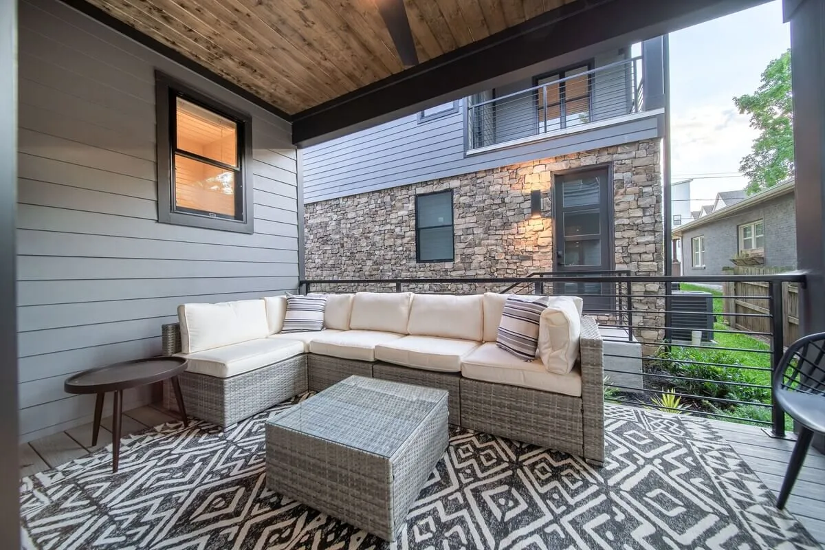 A spacious outdoor patio includes a sectional sofa, modern coffee table, and textured rug, set up for comfortable socializing, reading, or simply unwinding. The space feels inviting and designed for relaxation or gatherings, with ample room for family or friends.