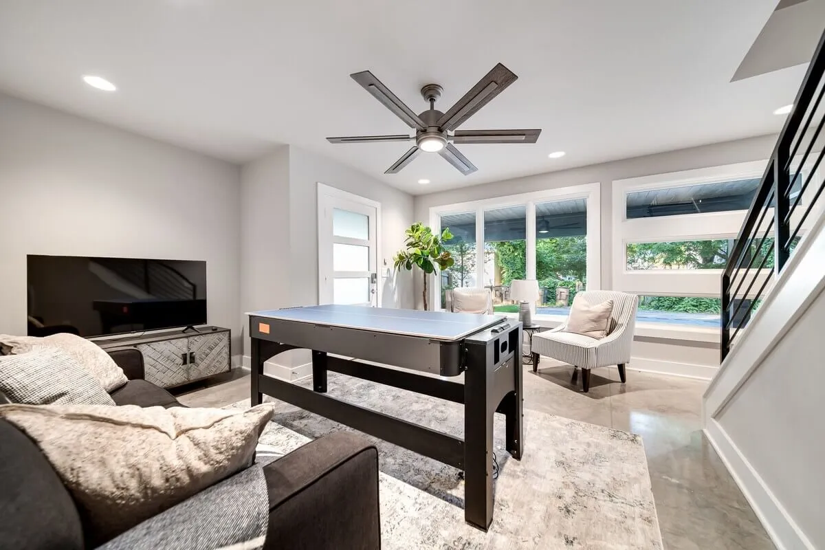 An entertainment-focused space with a contemporary pool table, a plush sofa, TV, and decorative plants by the window. The room is bright and airy, ideal for socializing, game nights, and relaxed afternoons with friends.