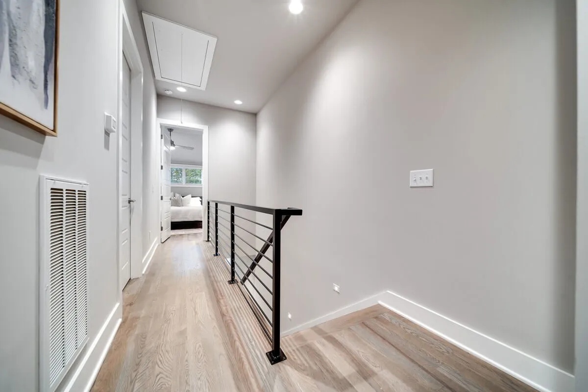 A welcoming entry area with a modern black railing, warm wooden flooring, and thoughtfully placed artwork on the wall. The space is bathed in natural light and designed for easy movement, evoking the first inviting steps into the home.