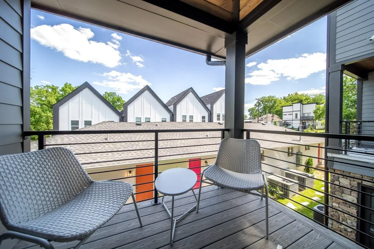 A tranquil balcony scene with two modern chairs and a small table, looking out over the neighborhood’s buildings. The intimate setup suggests a perfect spot to relax with a coffee or watch the sunset after city adventures.