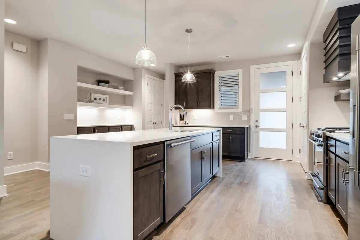 A bright kitchen scene featuring a central island, stainless steel appliances, pendant lighting, and dark cabinetry. The layout provides ample counter space for in-house chefs and a welcoming environment for group meal preparation.