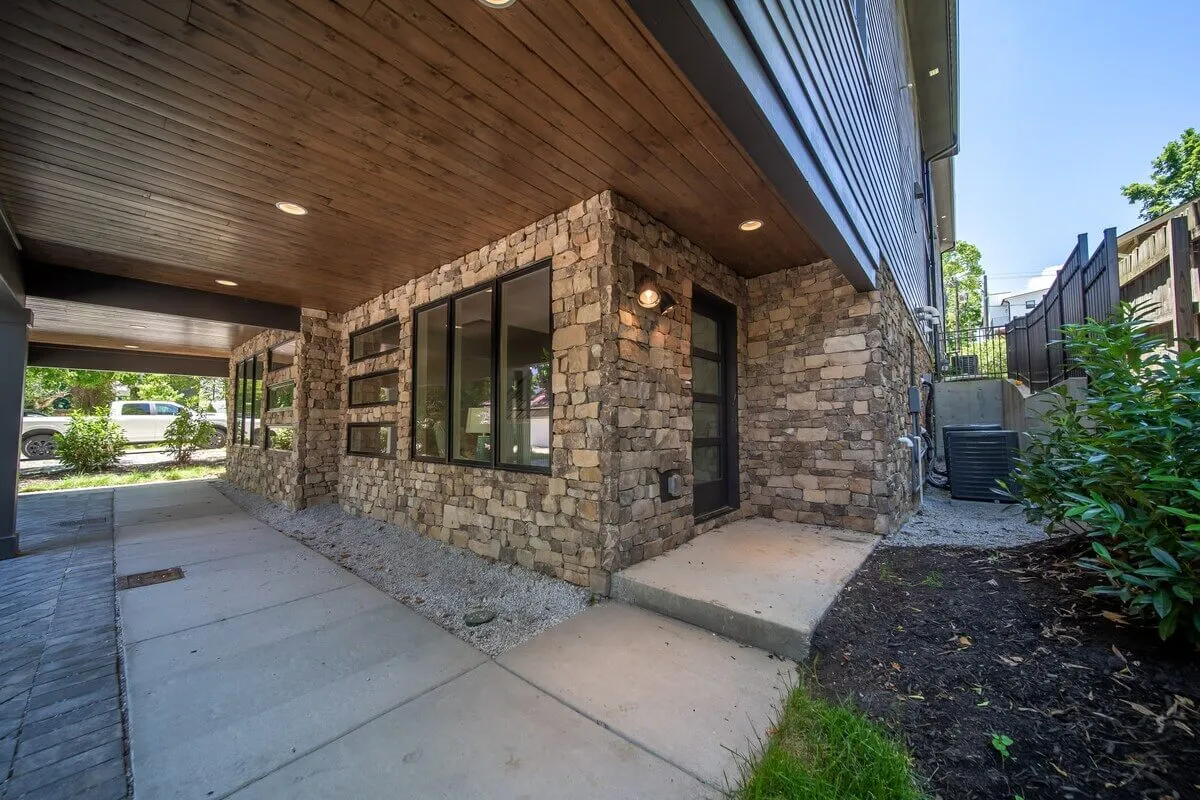 The image showcases the exterior of Sojourners Haven, featuring a welcoming stone wall, large windows, and a spacious entryway. The scene exudes an inviting atmosphere, perfect for first impressions and group arrivals.