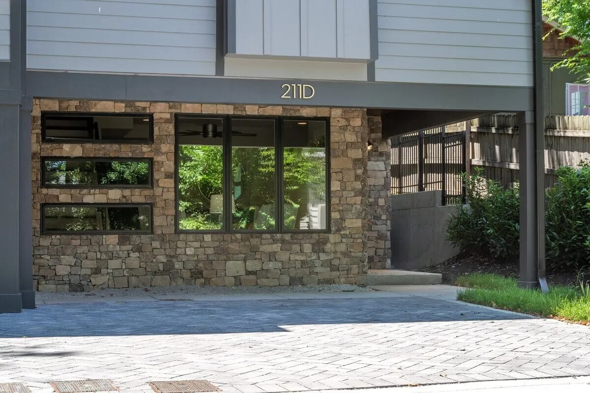 A welcoming exterior view of the property featuring a striking stone facade, expansive windows that hint at bright interiors, and the prominent house number 21D by the entry. The scene conveys a sense of arrival and the inviting nature of the home after a day in the city.